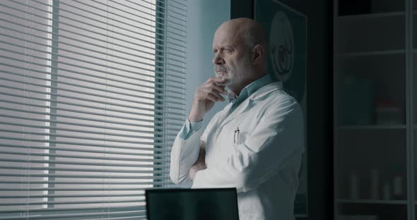 Pensive doctor standing next to a window