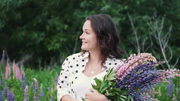 Young Beautiful Woman Posing in a Field with a Bouquet of Lilac Flowers, Happy Brunette in a Field alt