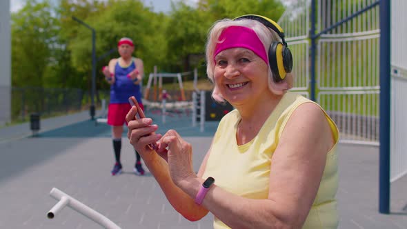 Senior Old Sportsman Grandfather with Headphones Listening Music From Mobile Phone on Playground alt