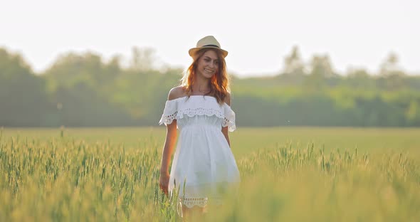 Happy Girl Walking in the Field with Rye and Smiling. Beautiful Young Woman Admires Nature alt