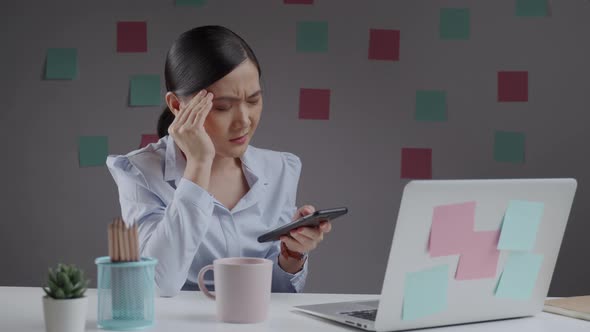 Asian woman reading news on smart phone has headache.