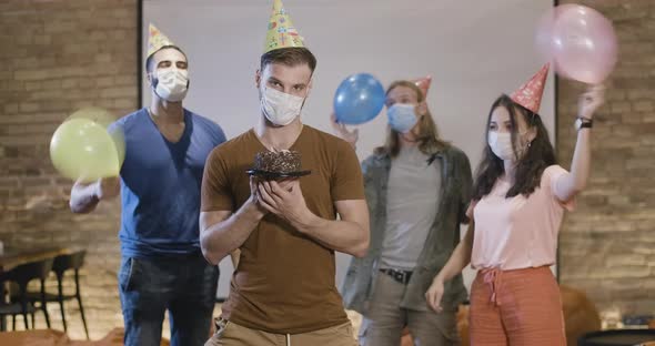 Portrait of Young Man in Covid-19 Face Mask Standing with Birthday Cake and Looking at Camera As alt