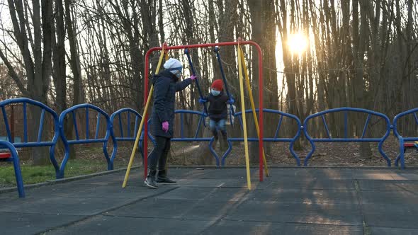 A mother swings a boy on a swing in medical masks .