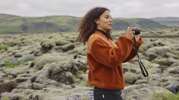 Smiling Young Woman Taking Photograph in Moss Covered Landscape alt