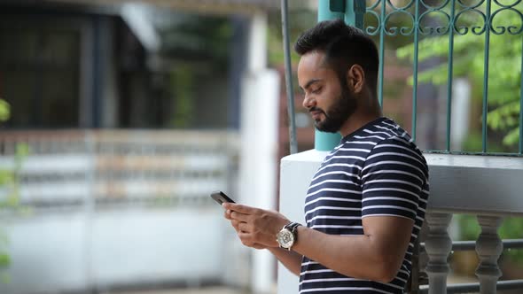 Young Happy Bearded Indian Man Using Phone and Waving Hand Outdoors