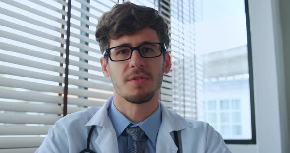Young male doctor looking at camera and talking while giving online medical consultation
