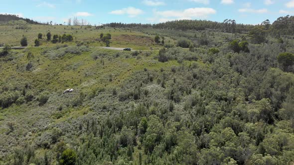 Aerial shot of a car parked at a mountain lookout with the wreckage of a car on the side of the moun alt