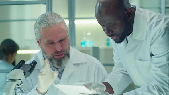 Multiethnic Lab Scientist Discussing Something on Tablet alt