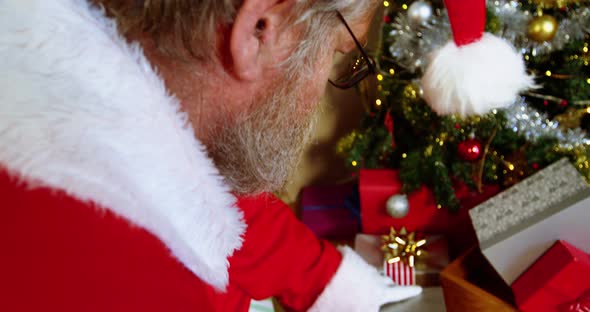 Santa claus placing gift box near christmas tree 4k alt