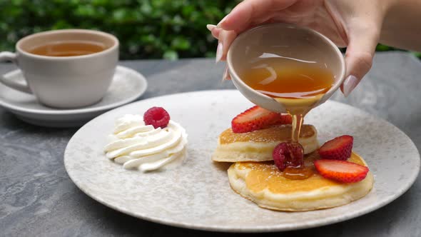 Woman Hand Pouring Maple Syrup on American Pancakes with Fresh Berries alt