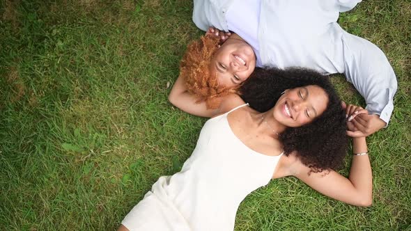 Young Beautiful Happy Lesbian African American Couple Lying on Grass Laughing Stretching Out Hands