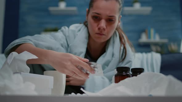 Woman with Cold Looking at Tablets with Capsules and Bottles with Pills alt