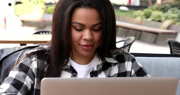 Young african american woman sitting in outdoor cafe and using laptop.