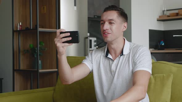 Smiling Young Man Making Video Call While Sitting on a Couch at Home. Portrait of Male Doing a Video alt