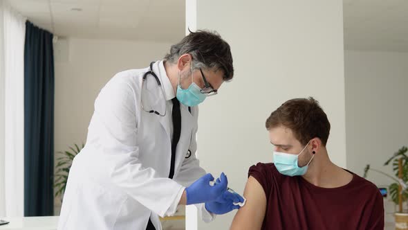 Senior Doctor Giving Covid19 or Flu Antivirus Vaccine Shot to Young Male Patient Wear Face Mask alt