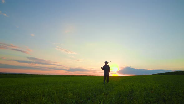 Silhouette of a Male Farmer Working in the Field at Sunset with a Shovel Walks Through Farmland alt