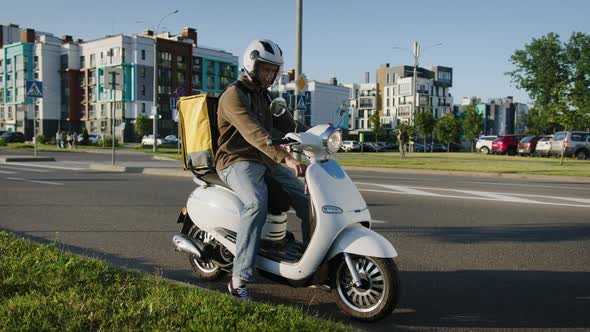 A Male Courier with a Thermos Bag Stops Along the Road to See the Exact Address of the Client