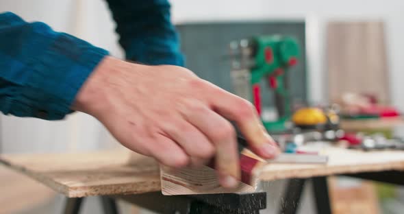 A Bearded Handyman is Sanding Wood for Furniture in a Carpentry Workshop alt