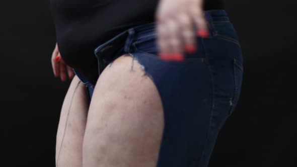 Fat Woman with Cellulite Trying to Put on Jeans on Black Background