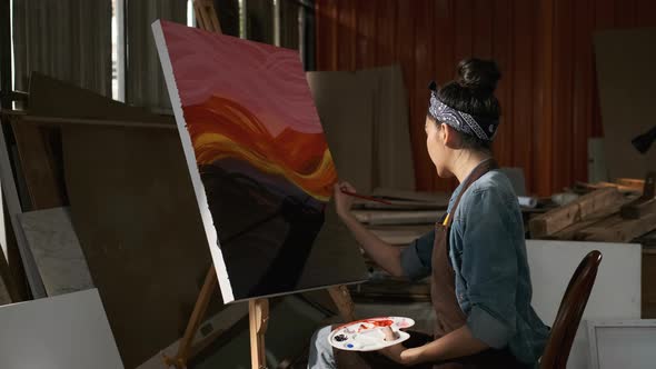 Asian Female Artist Draws create art piece with palette and brush painting at studio.