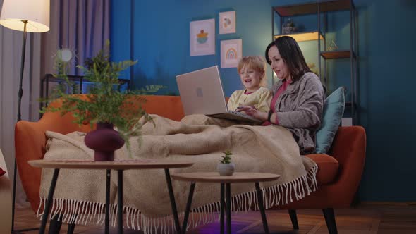 Mother and Small Child Daughter Kid Study at Laptop Watching Funny Movies Relaxing Lying on Sofa alt