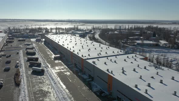 Trucks stand near a large warehouse loading cargo. Shooting from the air