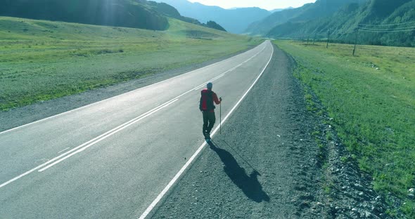 Flight Over Hitchhiker Tourist Walking on Asphalt Road. Huge Rural Valley at Summer Day. Backpack alt