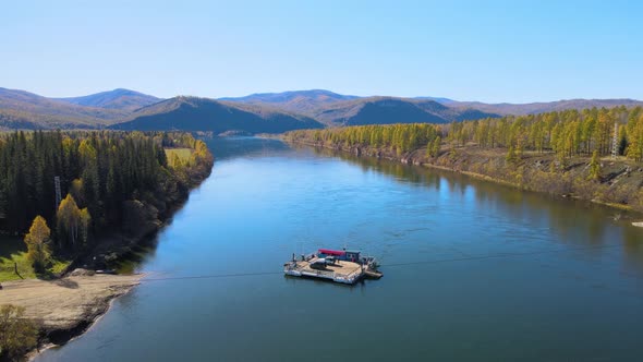 The ferry transports cars across the blue Yenisei River against the backdrop of mountains. alt