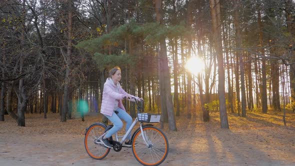 Slow Motion Young Woman Riding Bicycle in Autumn City Park at Sunset
