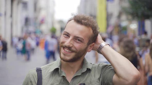 Charming young man walking on crowded street looking at camera. alt