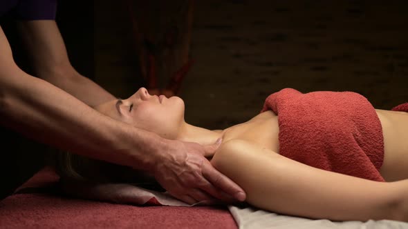 A man masseur kneads the shoulders of a young woman on a massage table alt