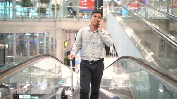 Young man with suitcase standing on the moving walkway while using smartphone.