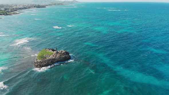 Flight over a lonely little island in the blue ocean near the shore line