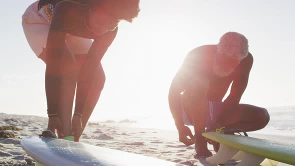 Happy african american couple preparing before surfing on sunny beach alt