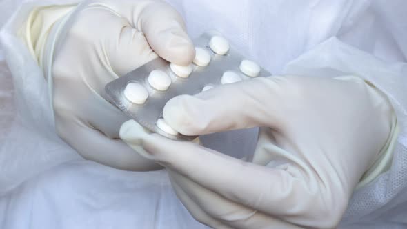 woman's (doctor, nurse) hands in gloves taking out pill from blister pack. medical assistant alt