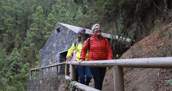 Multiracial women having fun during trekking day in to the wood with stone house in background alt