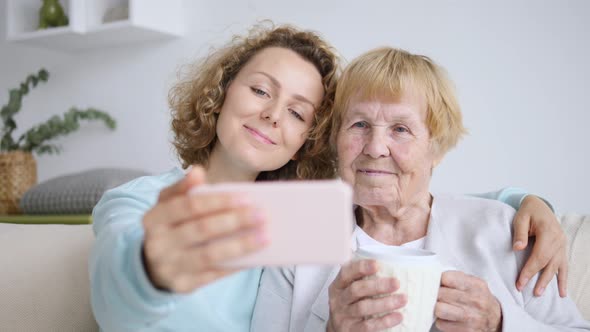 Grandmother And Granddaughter Taking Selfie Photo On Smart Phone Indoors alt