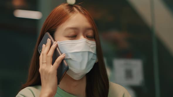 Young Beautiful Asian woman wearing a medical protective face mask talking on a smartphone