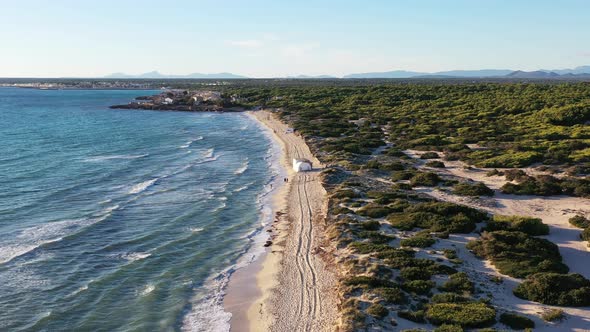 Trench Beach on Mallorca Island in Spain with people walking near a tent on the sand, Aerial flyover alt