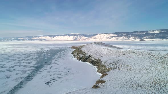 Aerial Over the Lands of Rocky Snow Covered Island in Lake Baikal Surrounded with Ice alt