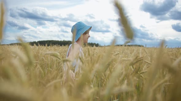 Teen Boy in a Blue Hat Running Across a Golden Wheat Field and Smiling