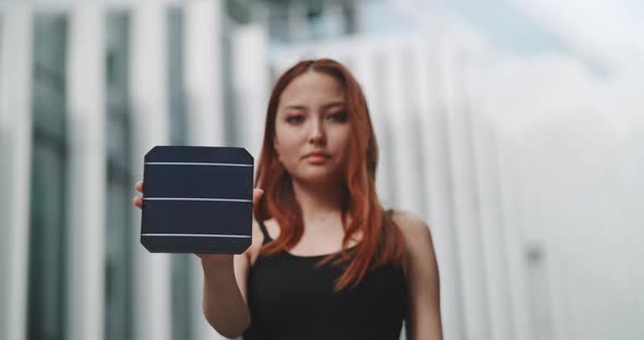 Young woman holding a solar cell while the wind is moving her hair alt