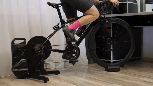 Woman is pedaling out of saddle on indoor smart bicycle trainer. alt