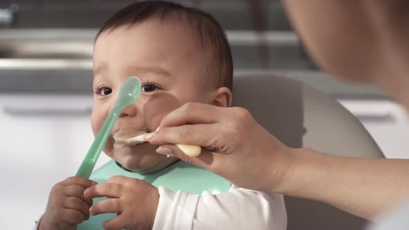 Sloppy 1-Year-Old Asian Baby Being Fed Puree alt