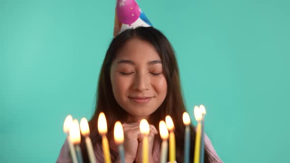 Happy Asian Woman Blowing Out Candles on Birthday alt