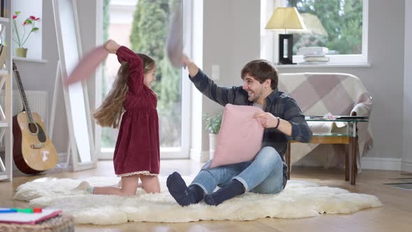 Wide Shot of Cheerful Father and Daughter Fighting Pillows at Home on Weekends alt