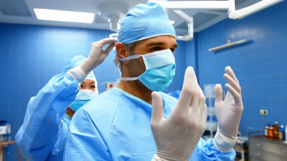 Nurse helping a surgeon in tying surgical mask alt