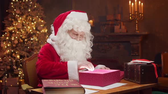 Workplace of Santa Claus. Cheerful Santa is working while sitting at the table. alt