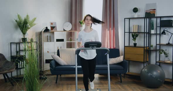 Active Confident Sportive 25-aged Woman Running on Treadmill in Cozy Apartment alt