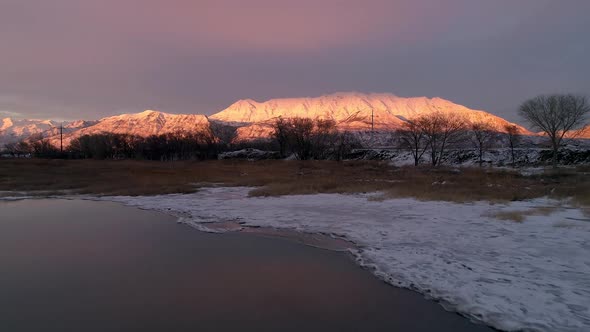 Flying backwards over icy shore viewing mountain lit by the sun alt